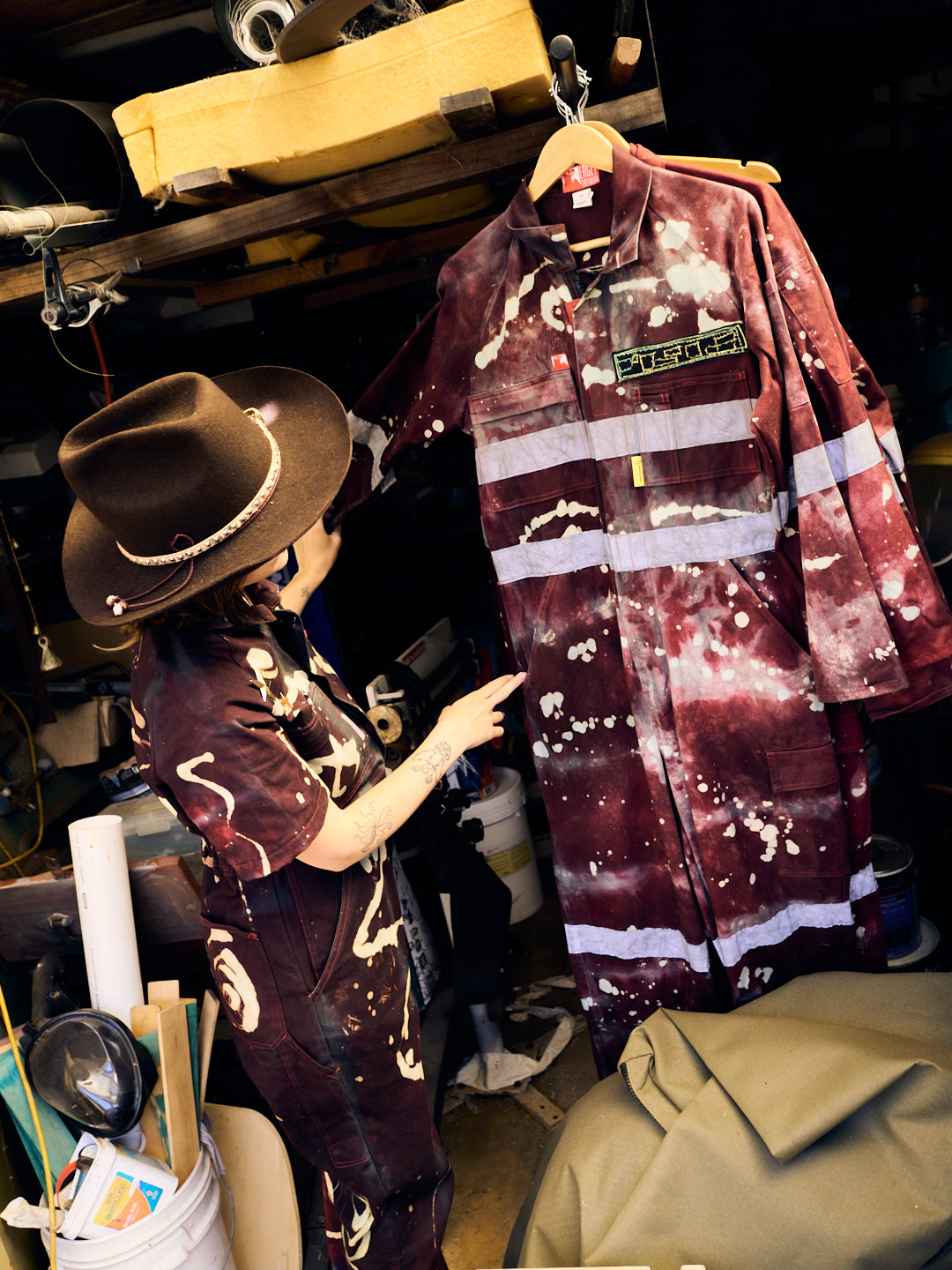 woman wearing cowboy at inspects a space suit with garbled name badge and hi vis strips. We use Oeko tex certified fibre reactive dyes. Our process uses rainwater and recycling, sunlight for drying and our workshop is powered by solar panels