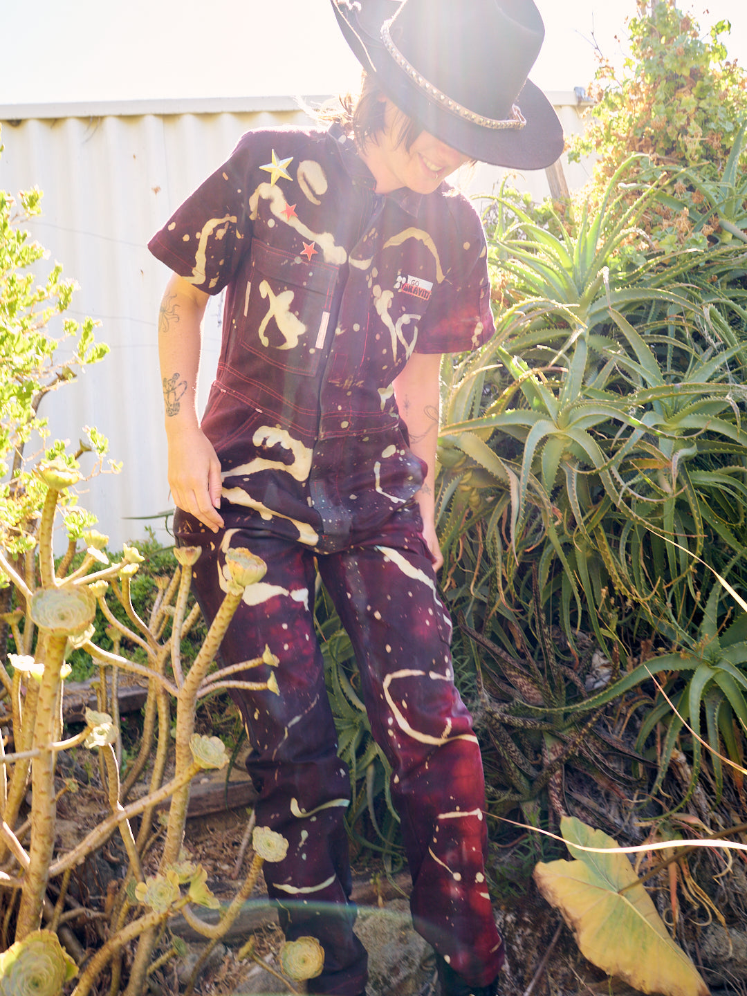 woman wears bleached and dyed maroon short sleeved jumpsiut with stars and a badge that reads GO Gravity