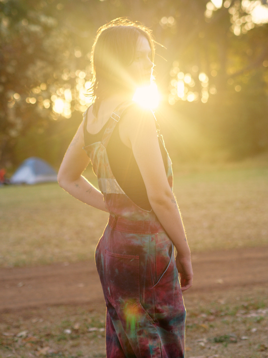 woman wearing tie dye overals with sunlight through the trees